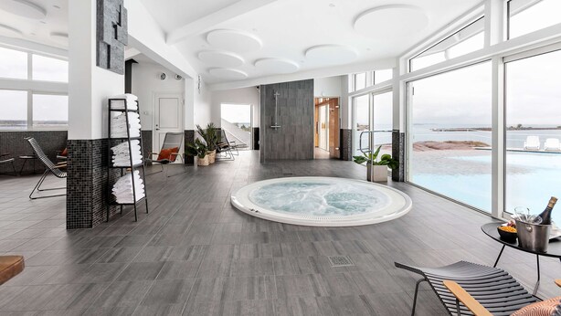 Ein großzügiger Innenbereich mit Whirlpool, Sitzgelegenheiten und großen Fenstern mit Blick auf das Meer.