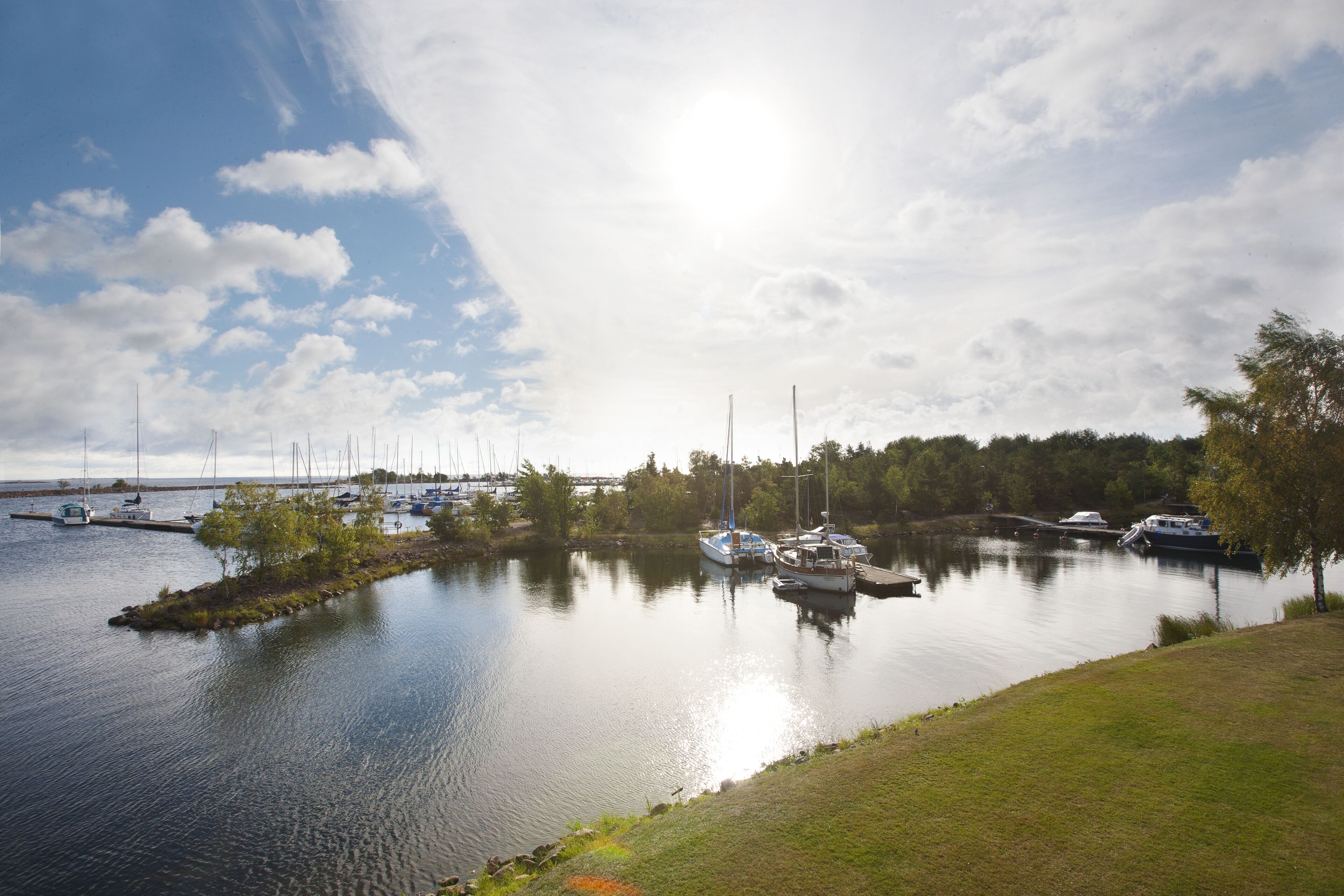 A calm lake with boats docked on the shore and a bridge in the background.