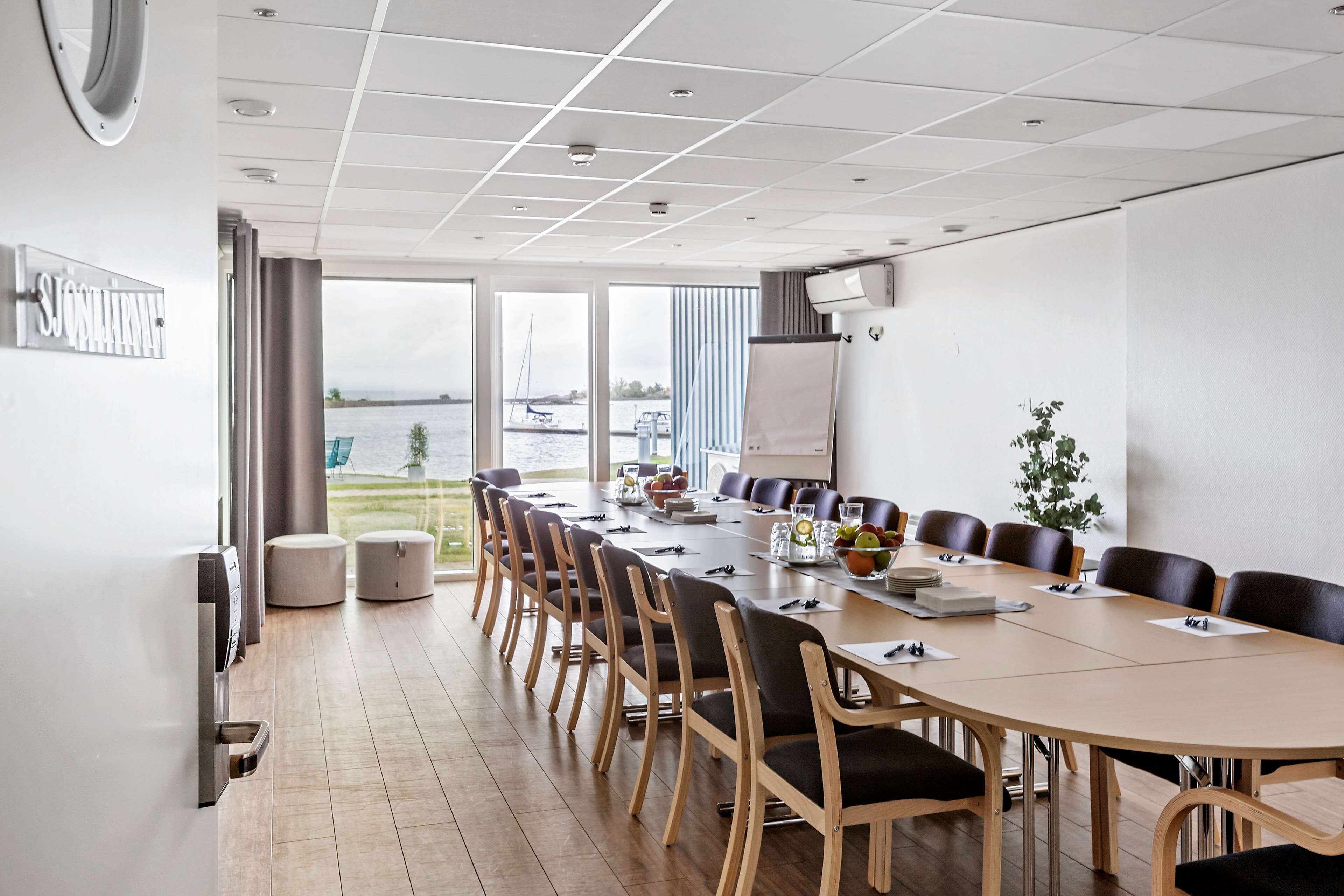 A conference room with a long table, chairs, a whiteboard, and a view of the water outside.