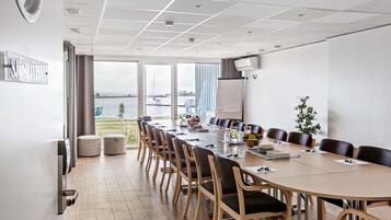 A conference room with a long table, chairs, a whiteboard, and a view of the water outside.