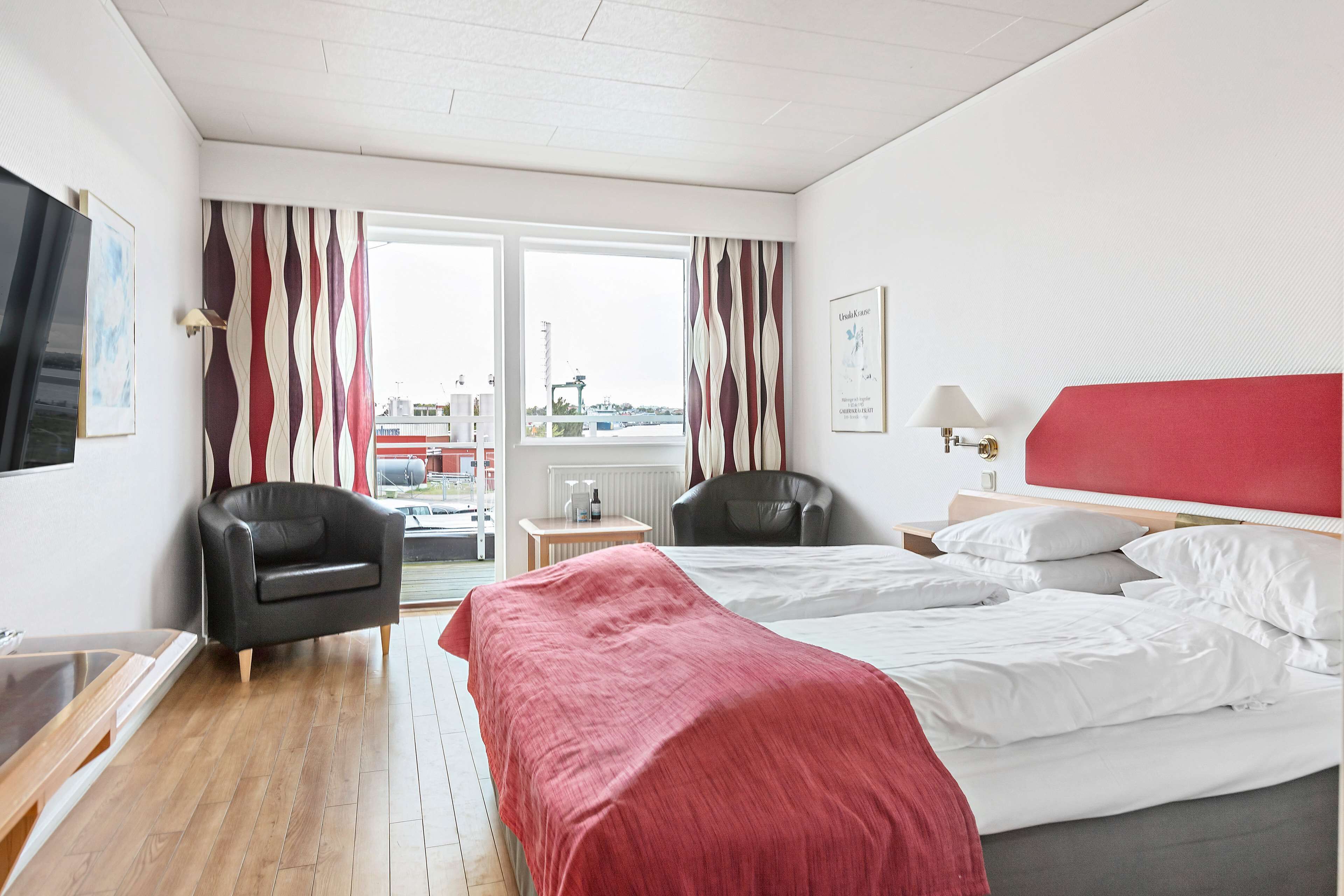 Habitació d'hotel amb llit, dues cadires, escriptori i finestra amb cortines.