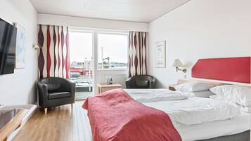 Una habitación de hotel con una cama, dos sillas, un escritorio y una ventana con cortinas.