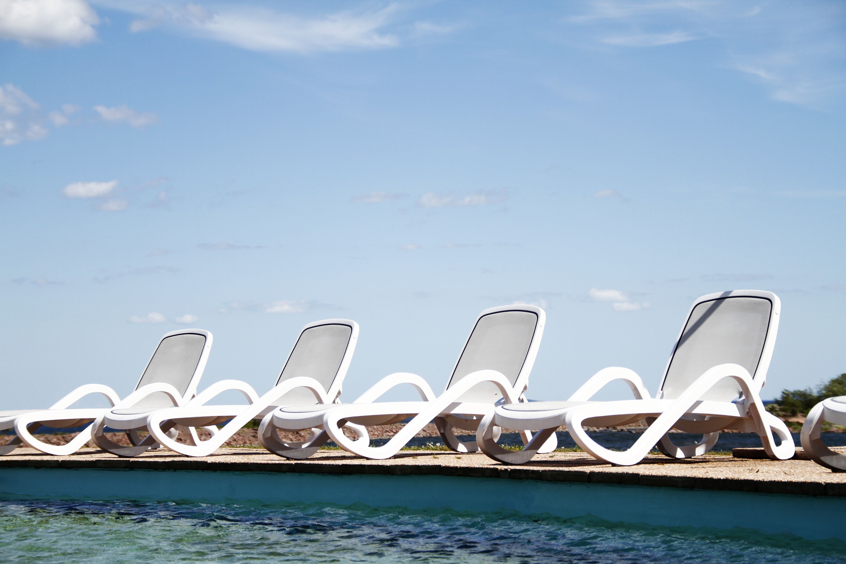 Une rangée de chaises longues blanches au bord d’une piscine.