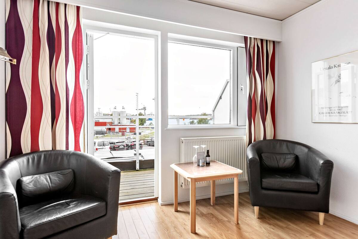 Une pièce moderne avec deux fauteuils en cuir noir, une table en bois et une vue sur le paysage urbain, visible à travers de grandes fenêtres.