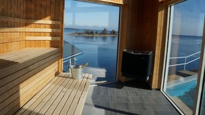 Eine Holzterrasse mit Sauna, eine Glastür zu einem Pool und Blick auf das Meer.