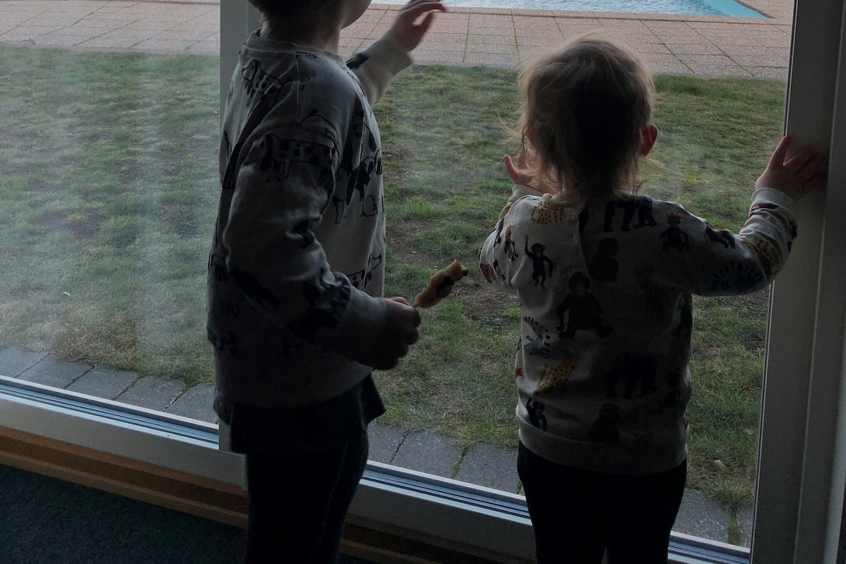 Deux enfants regardent par la fenêtre une piscine et une côte lointaine.