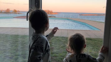 Two children looking out a window at a swimming pool and a distant shoreline.