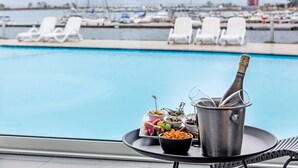 Ein Tisch am Pool mit einer Champagnerflasche, einer Schale mit Snacks und einer Serviertafel mit Essen.
