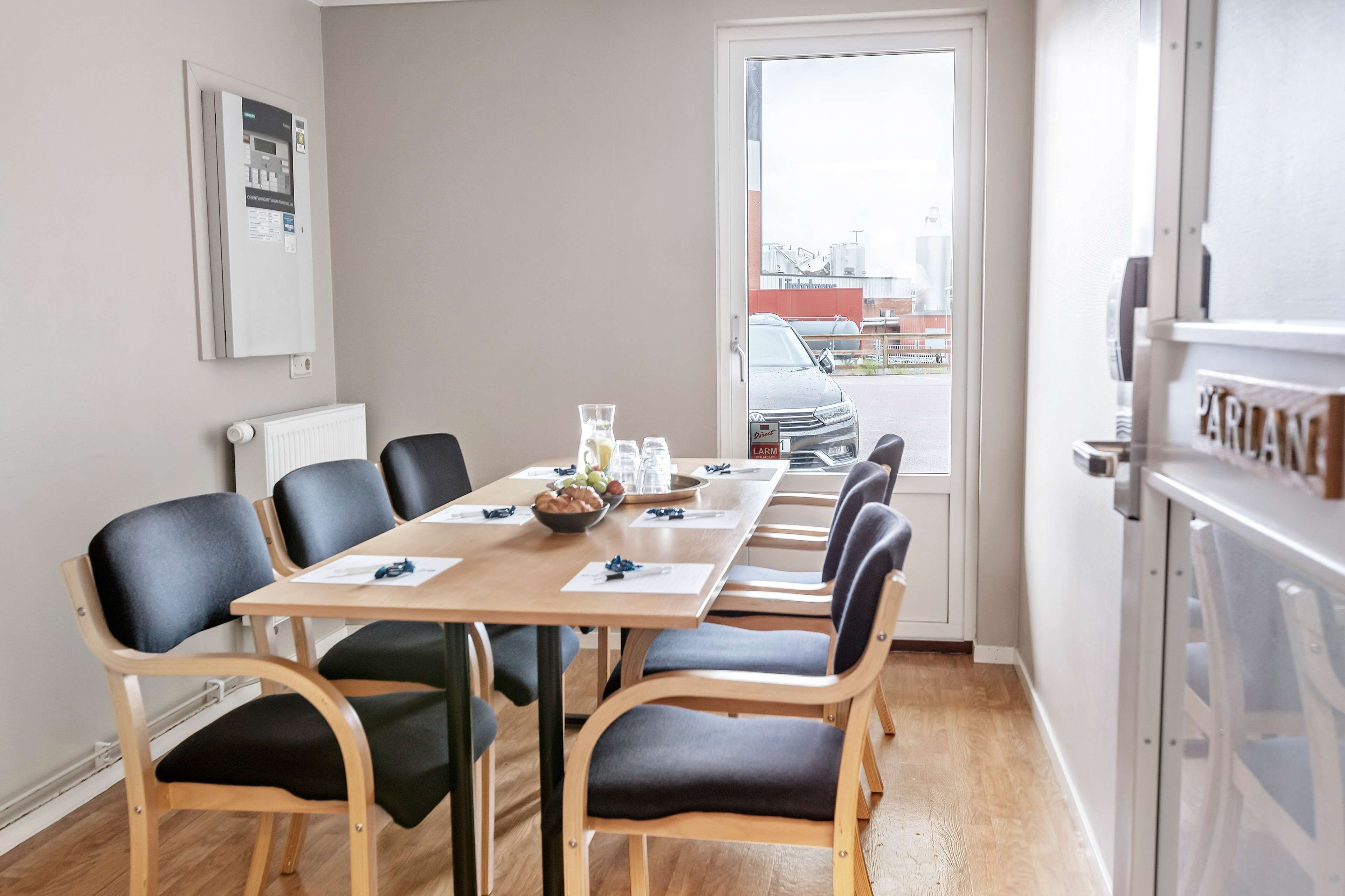 A conference room with a long table, black chairs, and a view of the outside through a door.