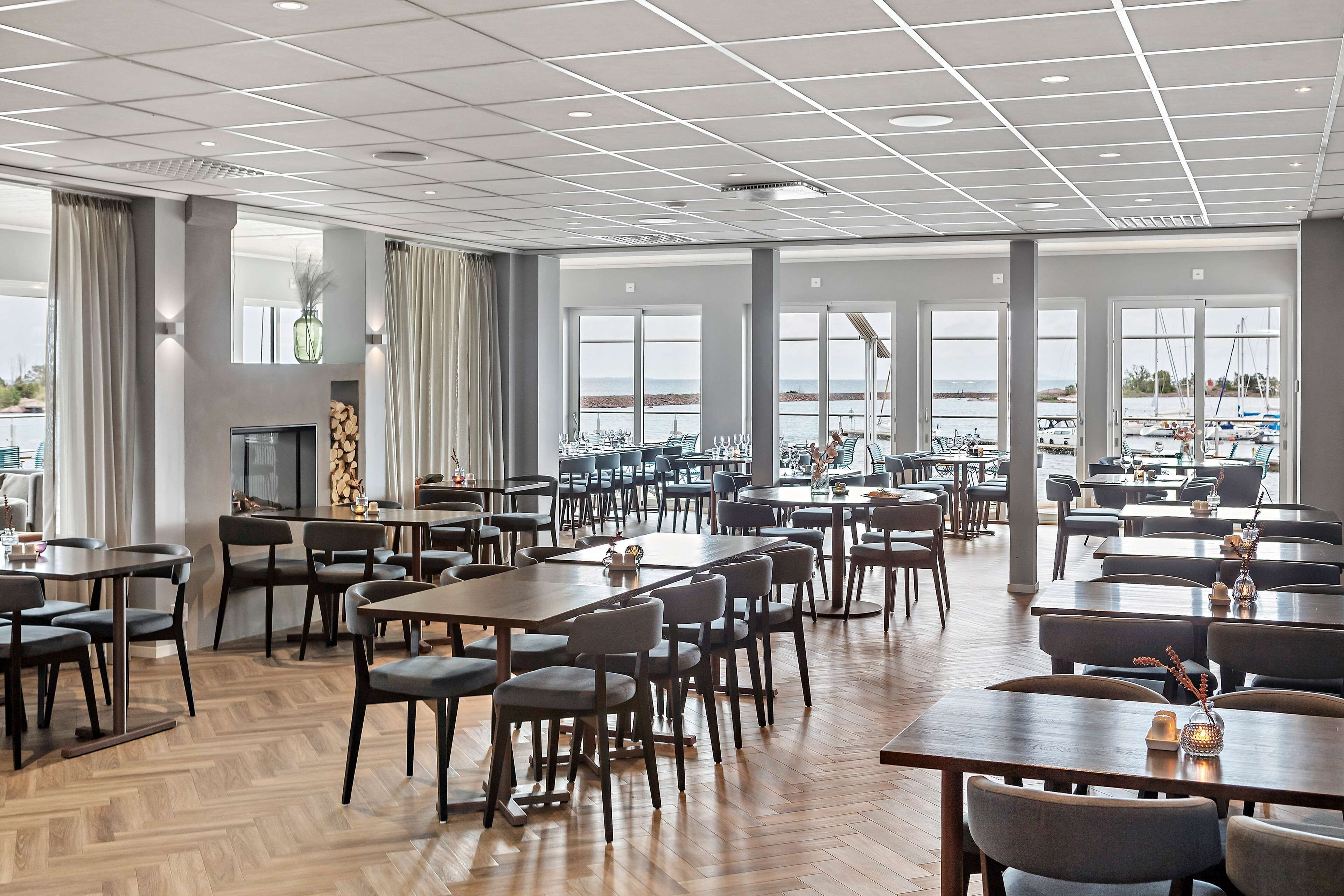 Un vaste espace dédié à la salle à manger, avec de nombreuses tables et chaises, de grandes fenêtres offrant une vue sur la mer et un design moderne au niveau du plafond.