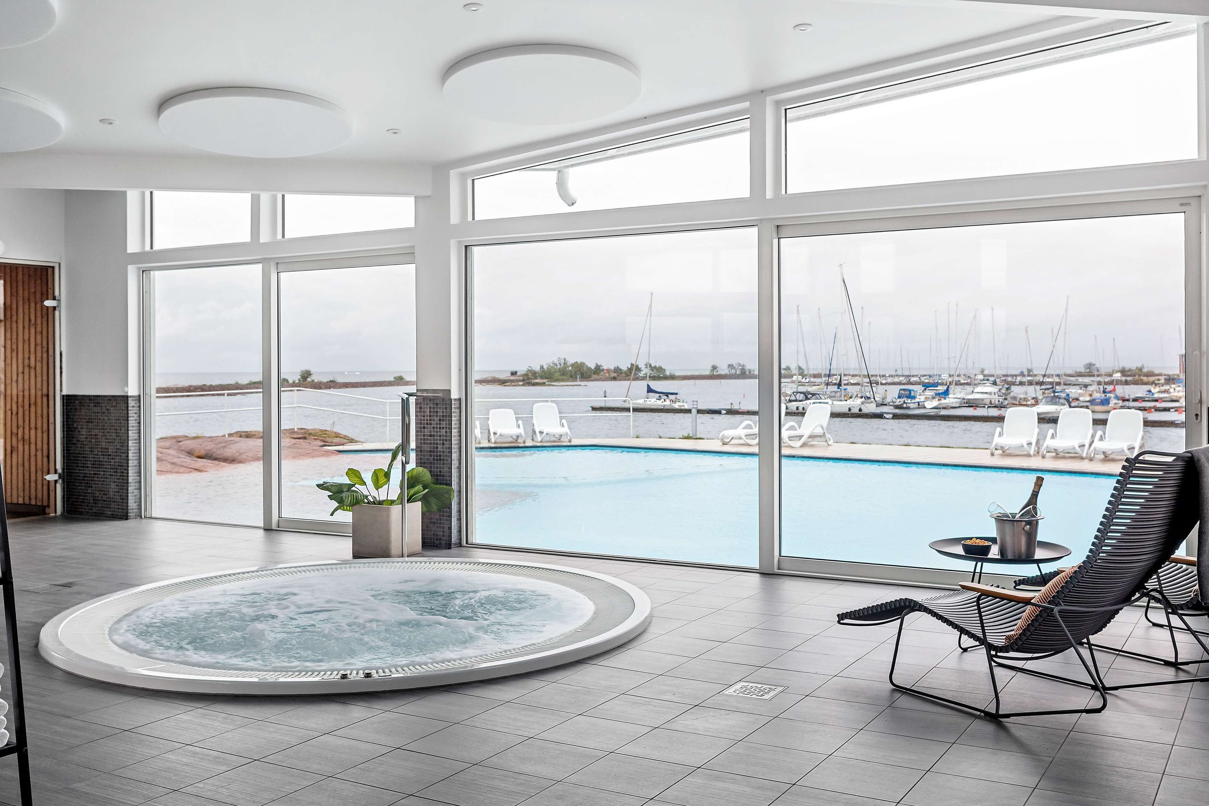 Un área de piscina interior moderna con un jacuzzi, sillas de descanso y vistas al puerto deportivo.