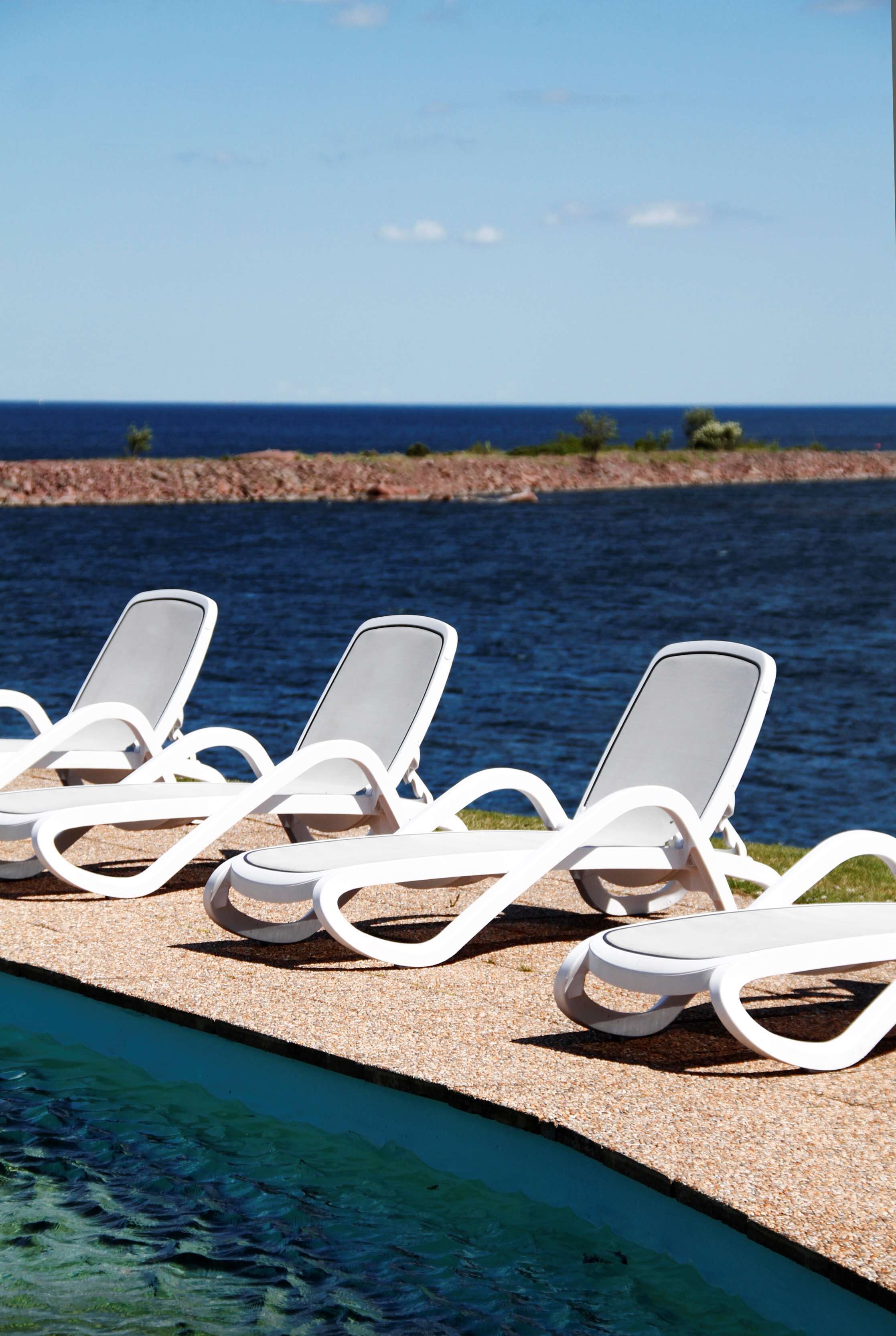 Una fila de sillas reclinables blancas junto a una piscina con vista despejada al océano.