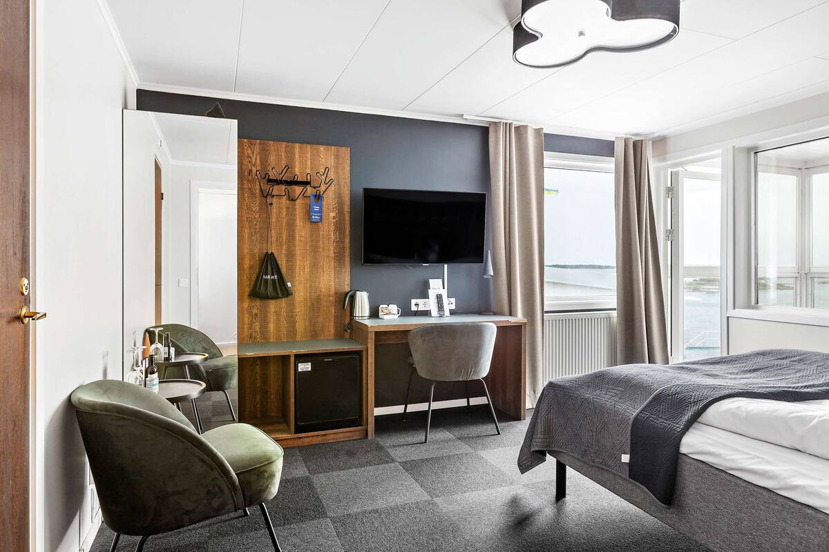 Une chambre d’hôtel avec un lit, un bureau, une chaise, une télévision et une vue sur la mer.