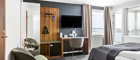 Habitación de hotel con cama, escritorio, silla, televisión y vista al mar.