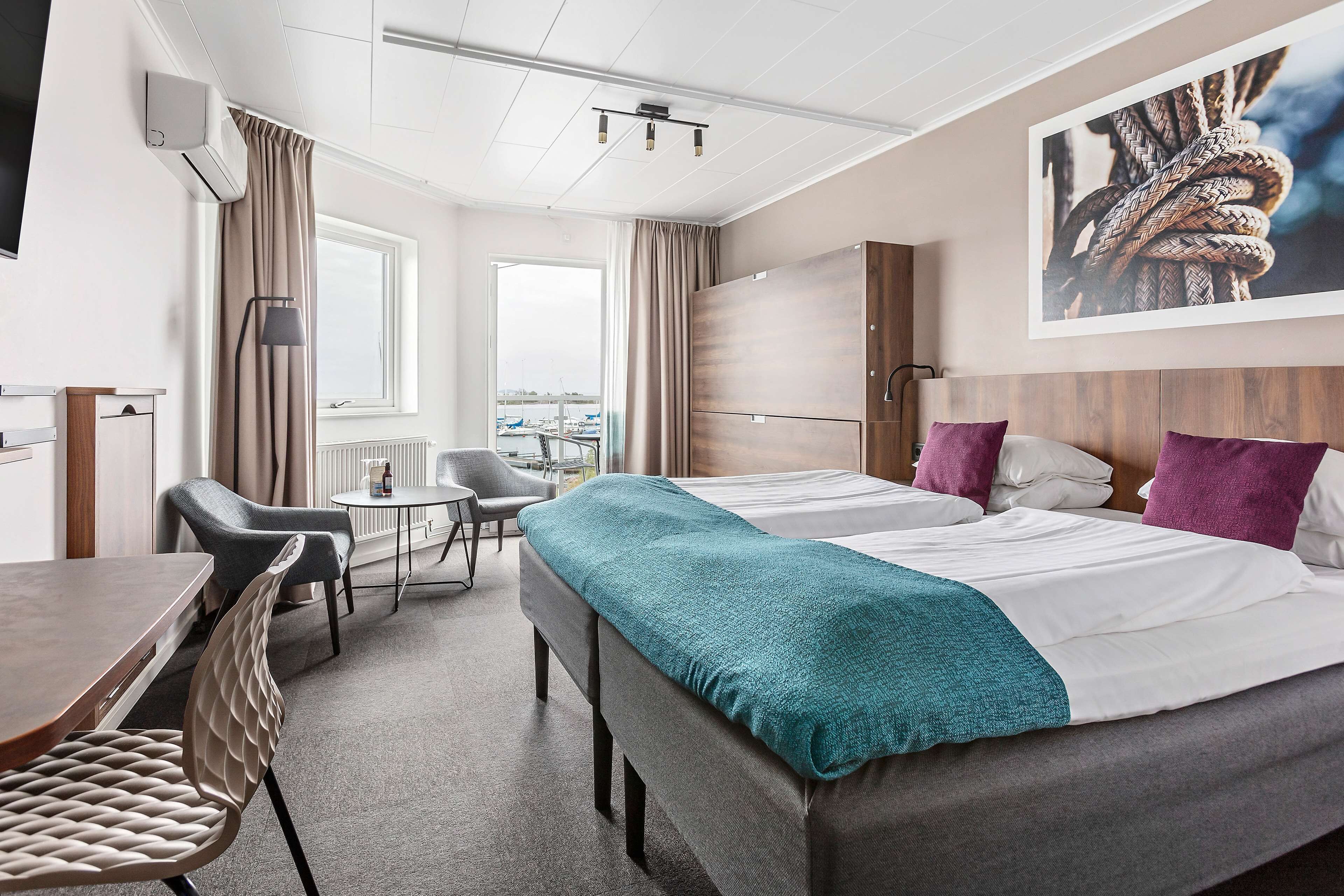 A hotel room with two beds, a desk, a chair, and a view of the city.