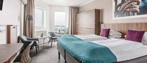 A hotel room with two beds, a desk, a chair, and a view of the city.