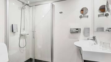 A modern bathroom with a glass-enclosed shower, a white sink with two glasses, and a mirror with a round frame.