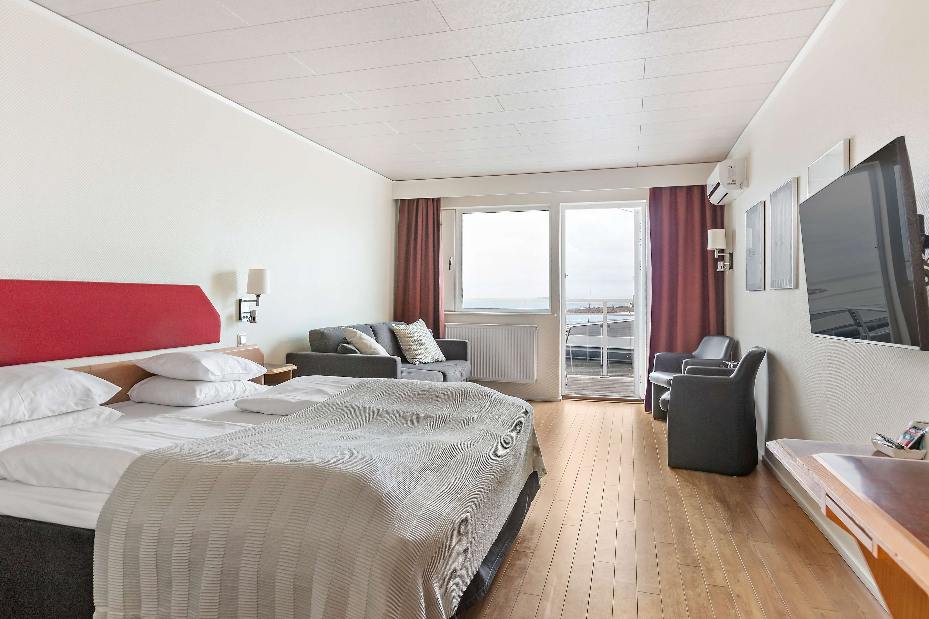 A hotel room with a bed, a desk, a TV, and a balcony with curtains.