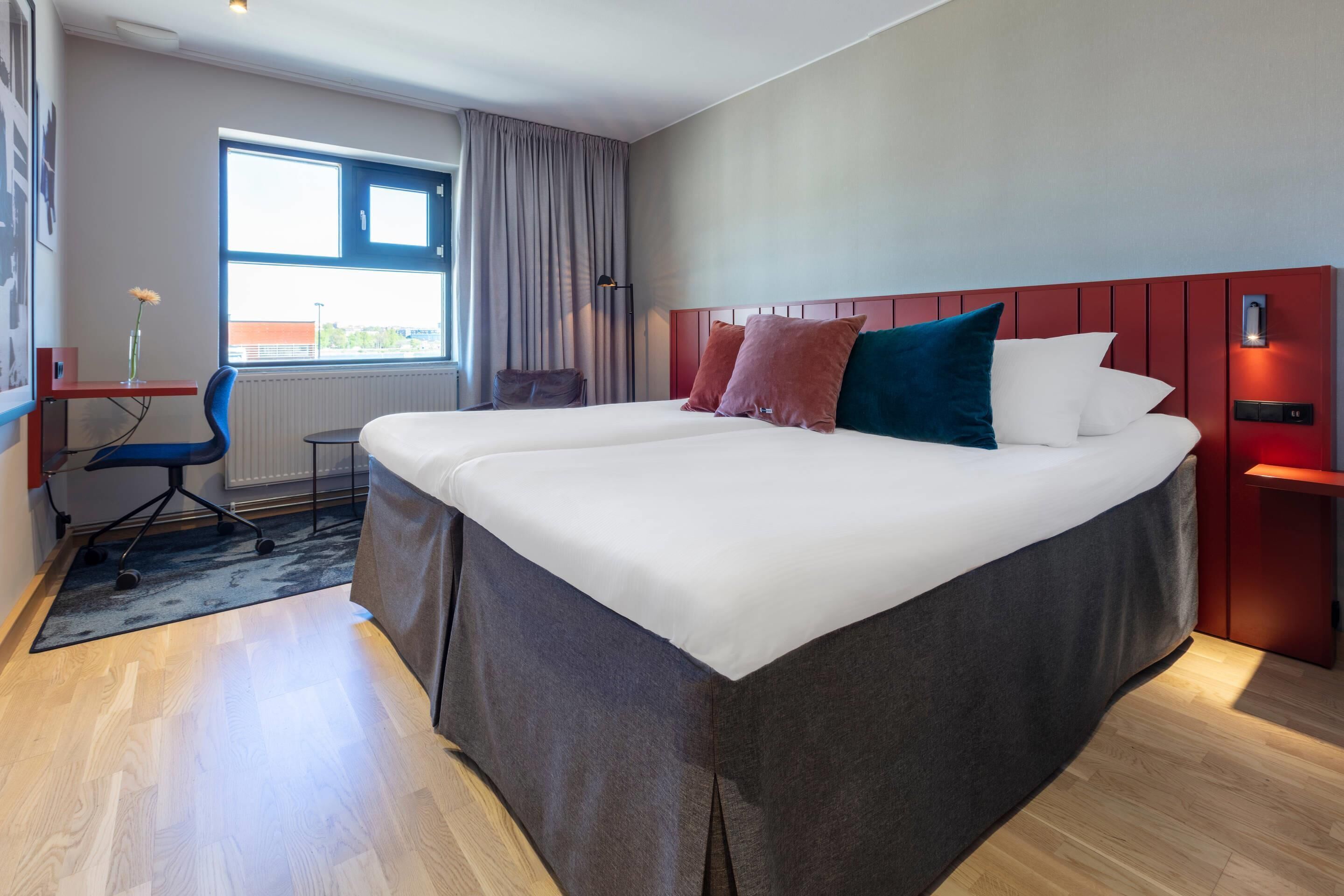 Una moderna camera d'hotel con un letto grande, una scrivania con una sedia e vista sull'esterno dalla finestra.