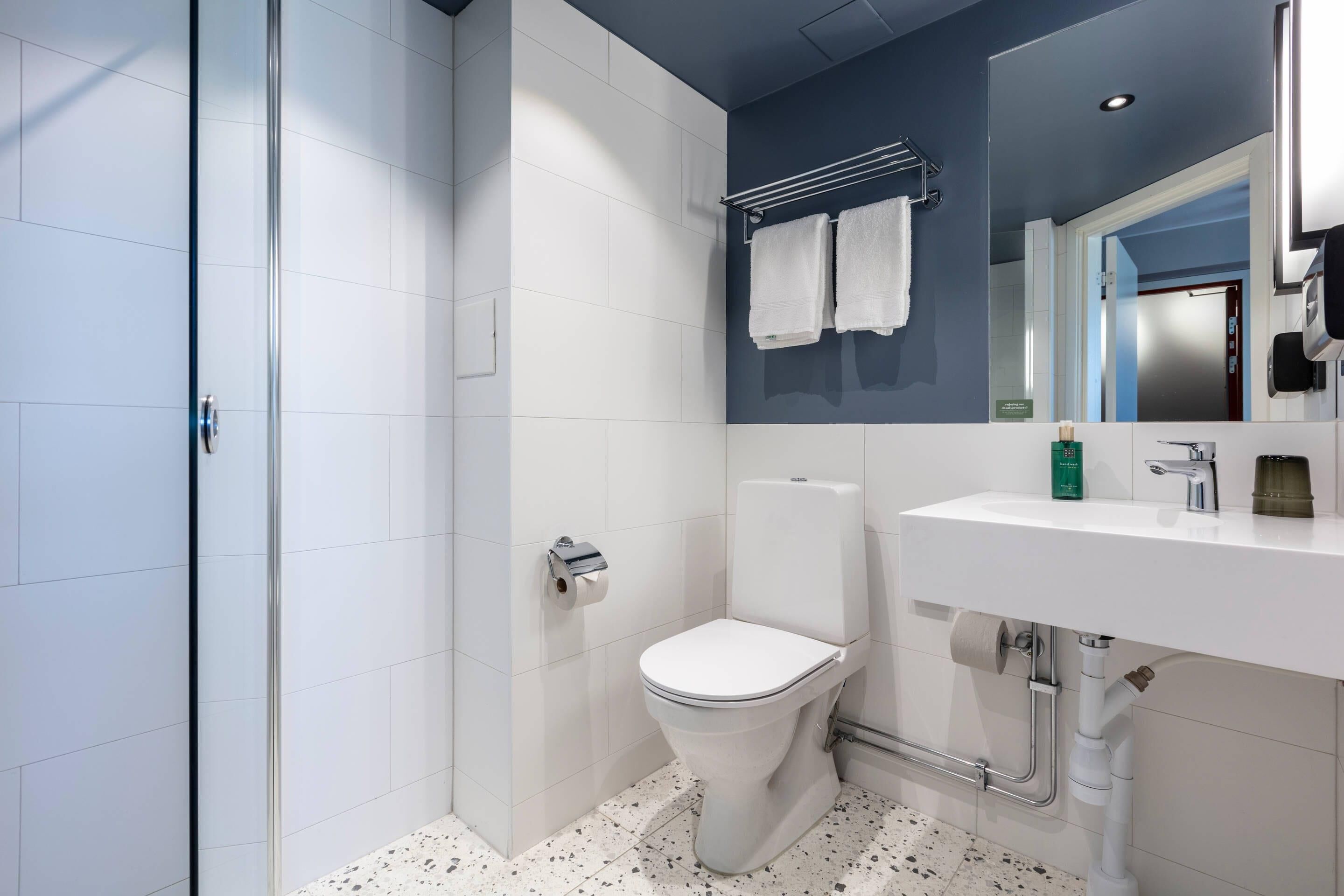 Un baño moderno con inodoro blanco, lavabo con espejo y zona de ducha con puerta de vidrio.
