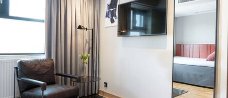 A modern room with a leather chair, a small table with a vase, a mounted TV, and a bed with a red headboard.