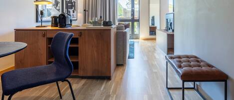 Una habitación de hotel moderna con un escritorio de madera, una silla azul, un banco y un amplio ventanal con vistas al exterior.
