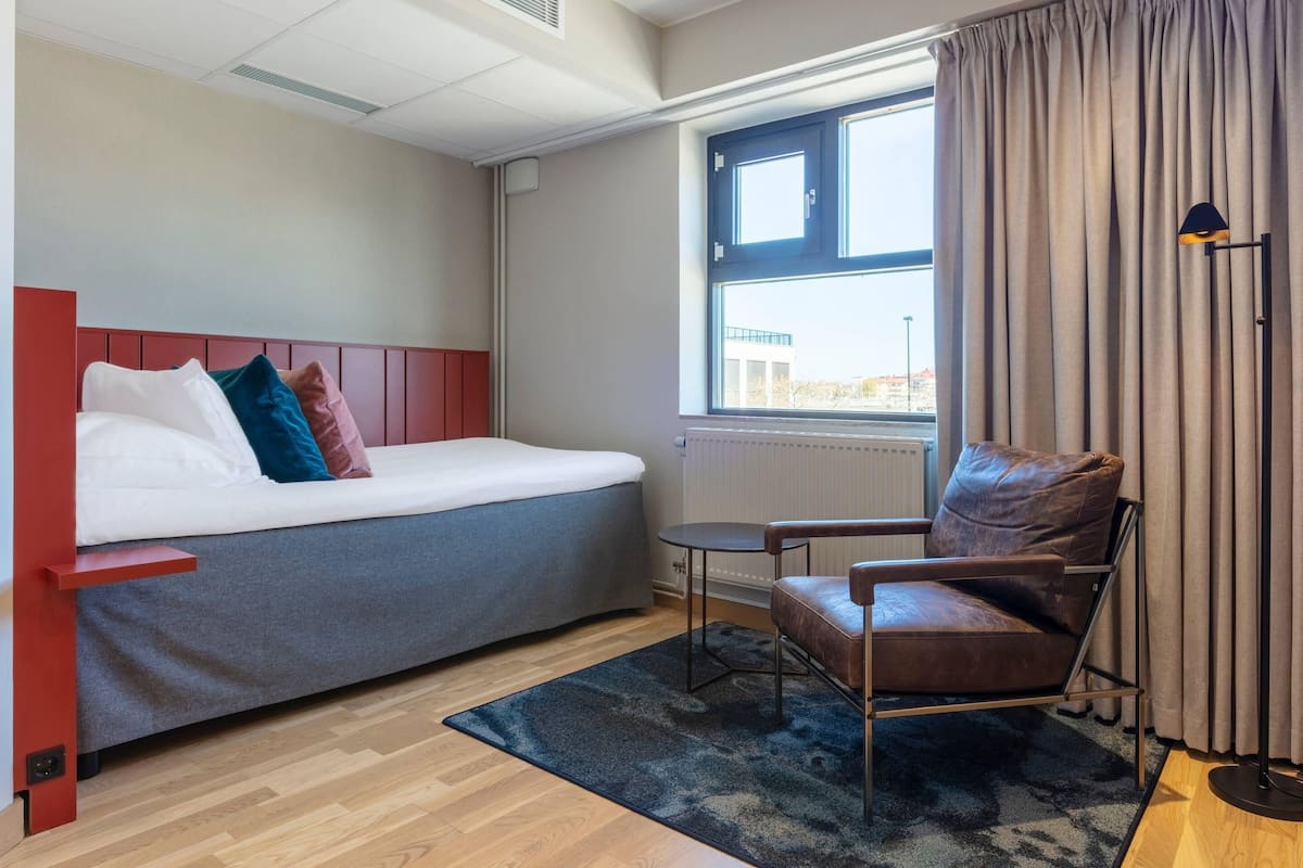 Ein modernes Hotelzimmer mit Bett, Stuhl, kleinem Tisch und einem fenster mit Vorhängen.