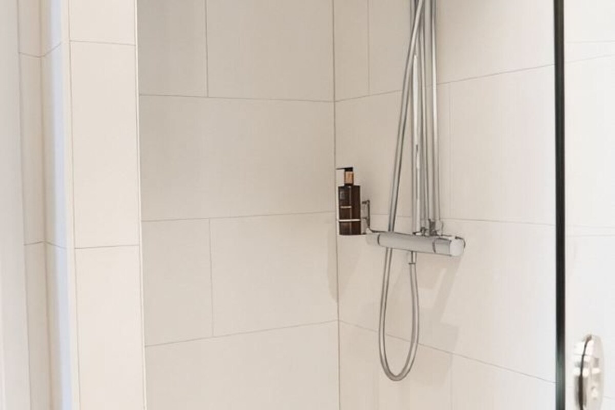 Une douche équipée d’un pommeau de douche à main et d’un panneau de commande fixé au mur.