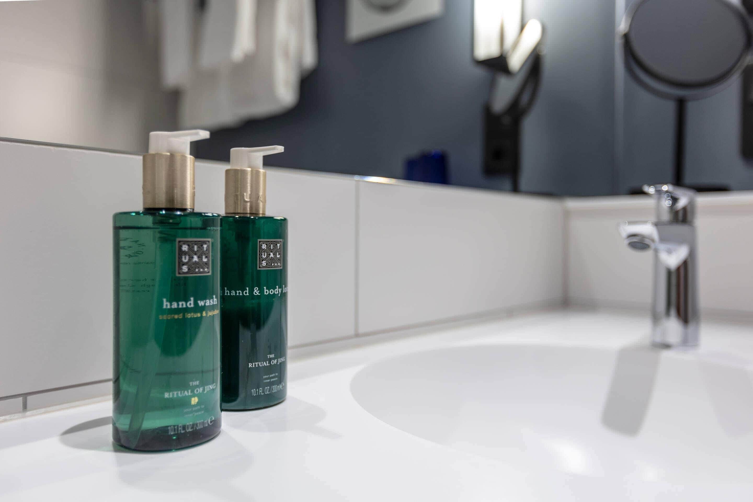 Un baño con un lavabo blanco, dos botellas dispensadoras de jabón verde y un espejo.