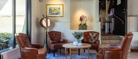 Una hall con poltrone in pelle, un tavolo rotondo, un quadro incorniciato e un vaso con fiori.