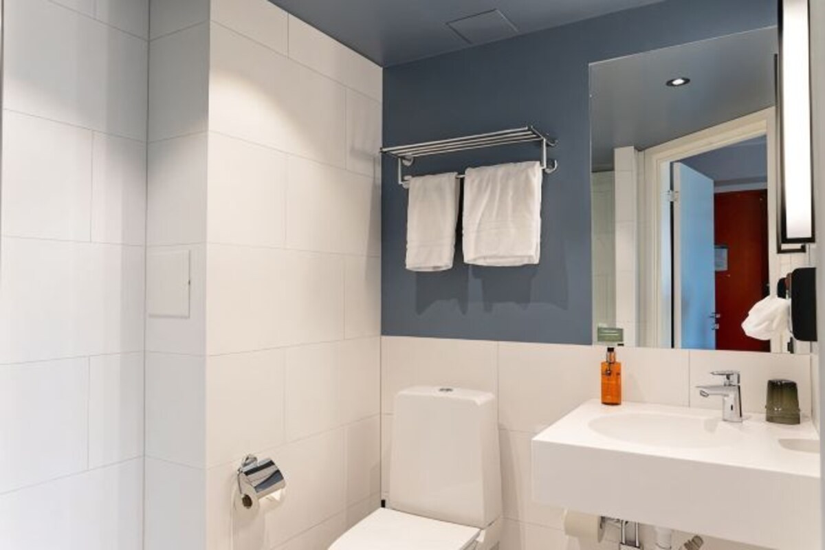 A bathroom with a white toilet, a sink, a mirror, and two towels hanging on a rack.