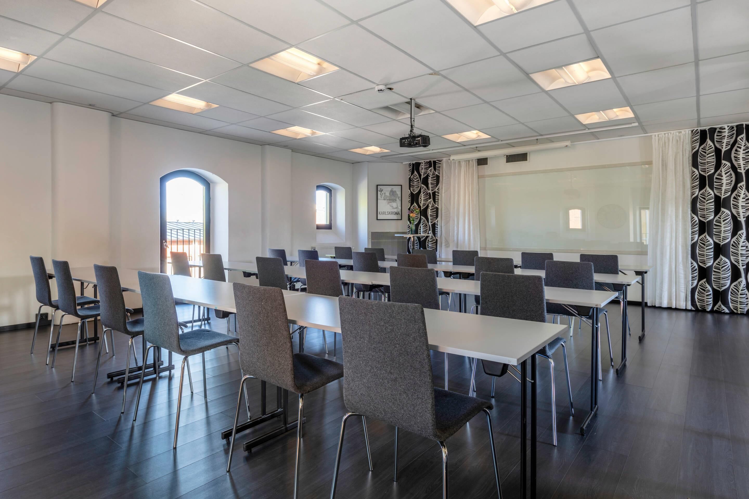 A conference room with tables and chairs, a projector, and a large screen.
