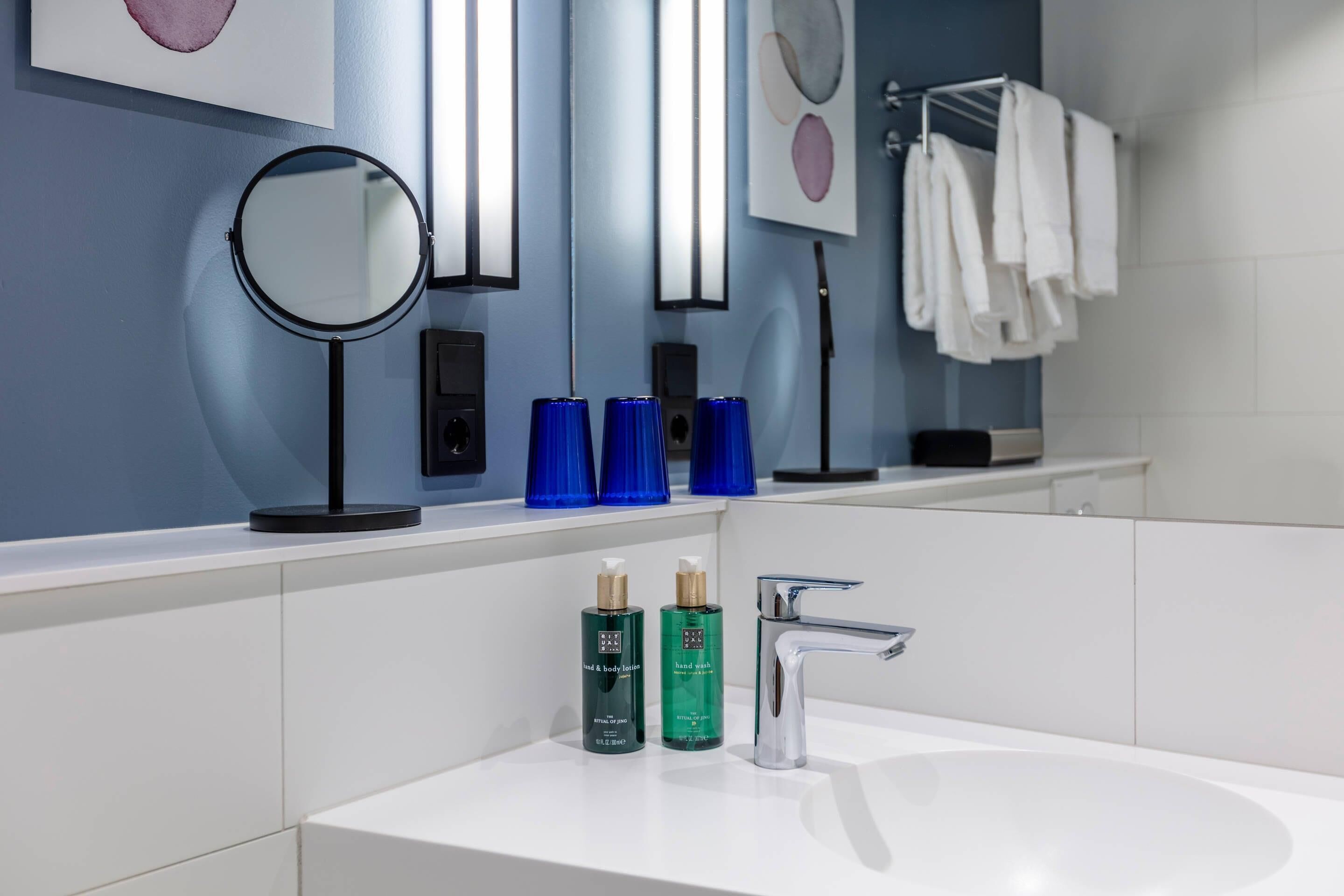 A modern bathroom with a white sink, a round mirror, and two blue soap dispensers.