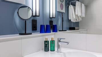 A modern bathroom with a white sink, a round mirror, and two blue soap dispensers.