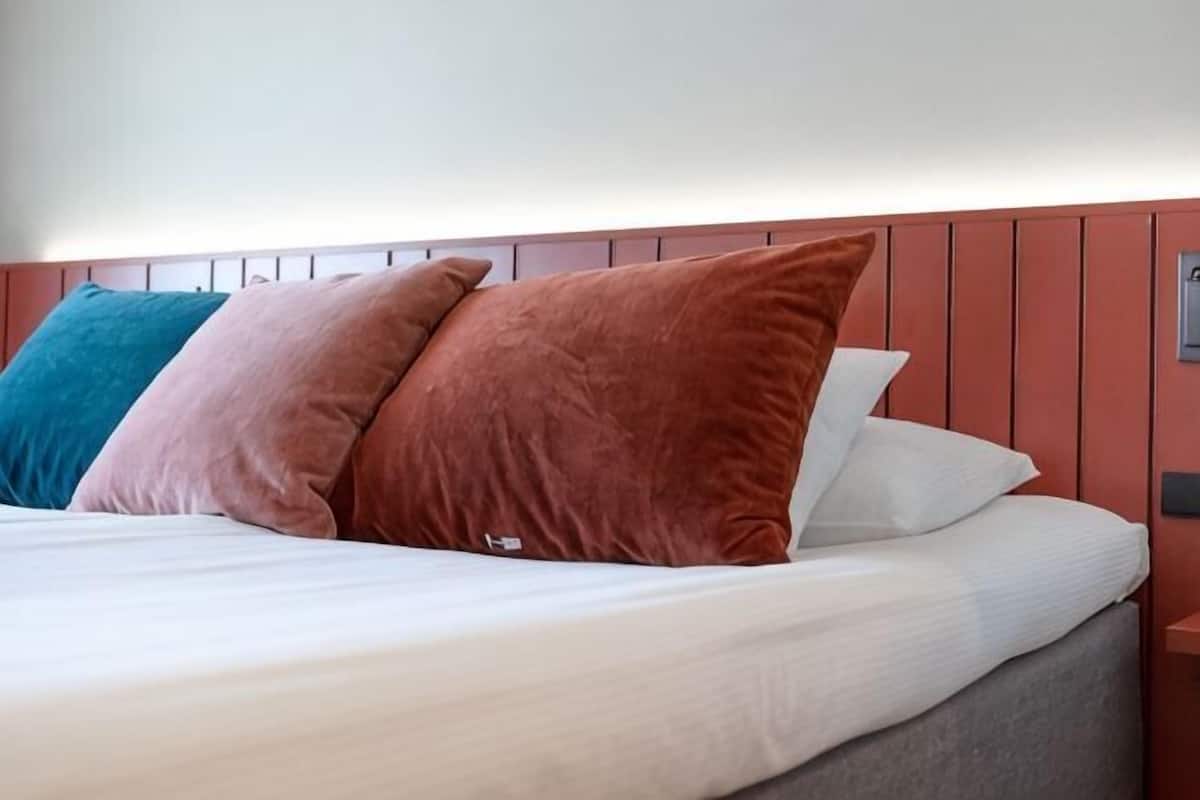Ein Bett mit Kissen, einem Kopfteil und einer wandmontierten Bedieneinheit.