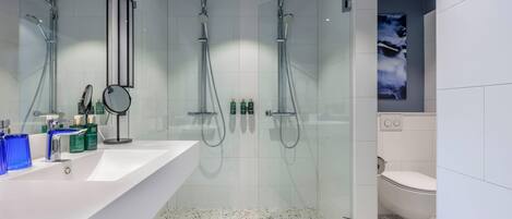 Un baño moderno con un lavamanos grande de color blanco, dos duchas de mano, una cabina de ducha con paredes de vidrio y un inodoro blanco.