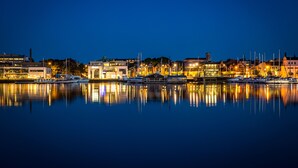 A waterfront marina at night with boats docked, buildings with illuminated windows, and a calm reflective water surface. - Home Hotel Carlscrona (Karlskrona)