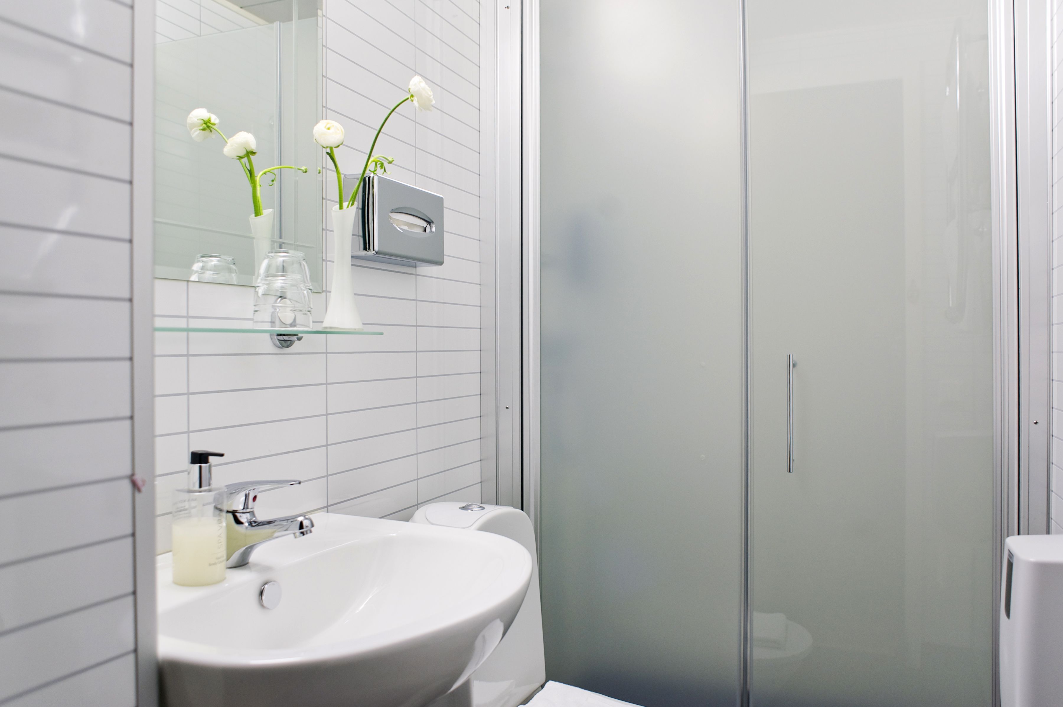 A modern bathroom with a white sink, mirror, and glass shower enclosure.