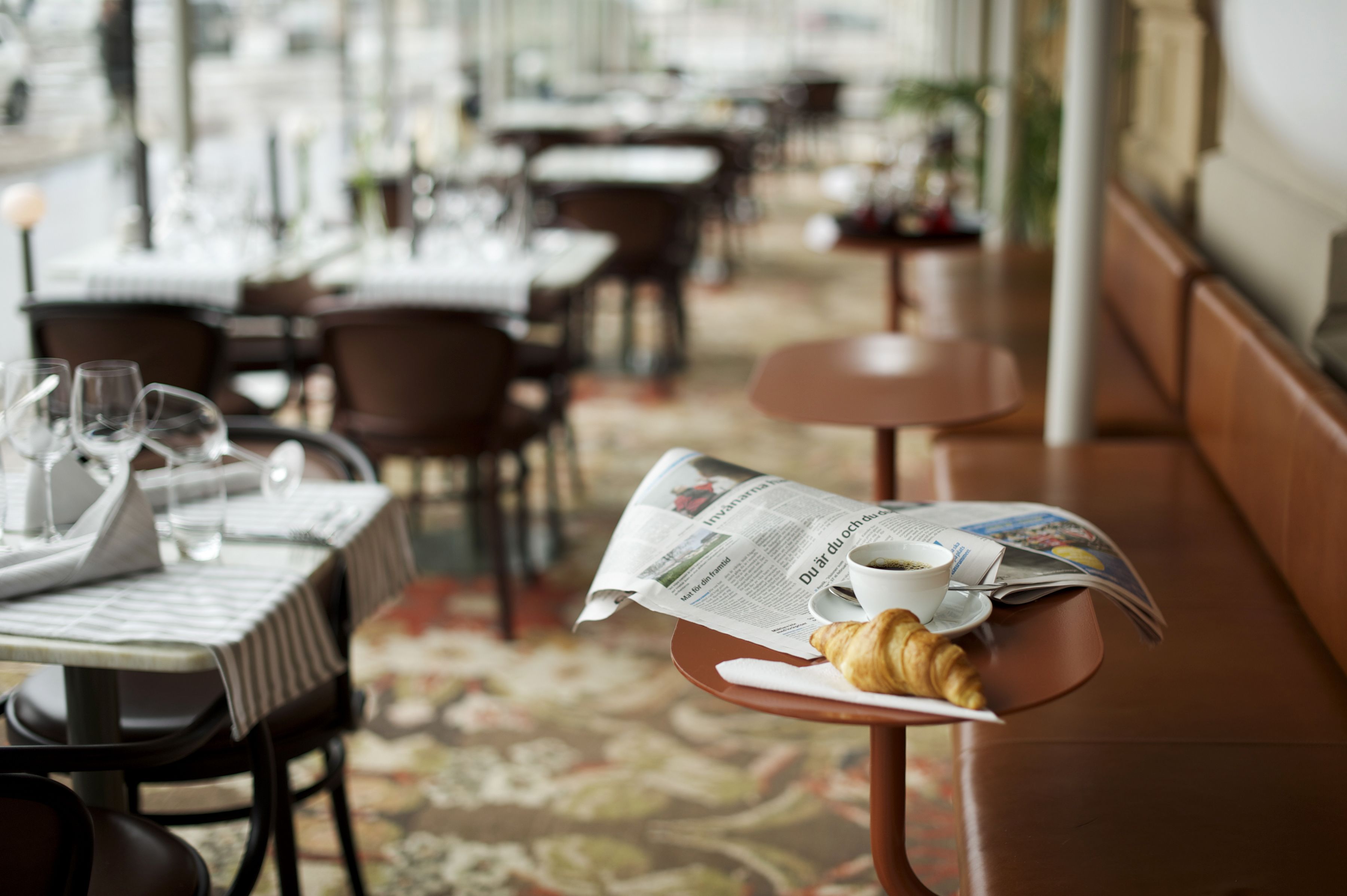 A dining area with tables set for meals, including a croissant and a cup of coffee on a small table.