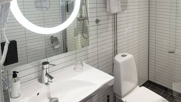 Un baño moderno con un lavabo blanco, un inodoro, una cabina de ducha de vidrio y un espejo redondo con luz.