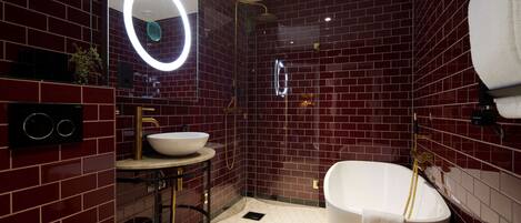 Un baño moderno con una bañera independiente, un espejo redondo con luz y un lavamanos con grifo dorado.