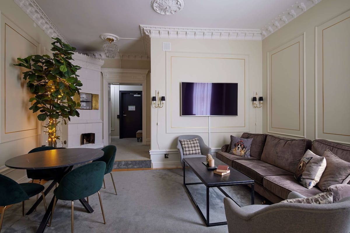 A living room with a round table, green chairs, a sofa, and a flat-screen TV mounted on the wall.
