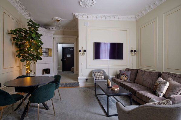 A living room with a round table, green chairs, a sofa, and a flat-screen TV mounted on the wall.