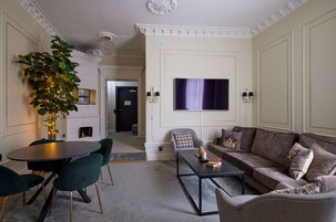 A living room with a round table, green chairs, a sofa, and a flat-screen TV mounted on the wall.