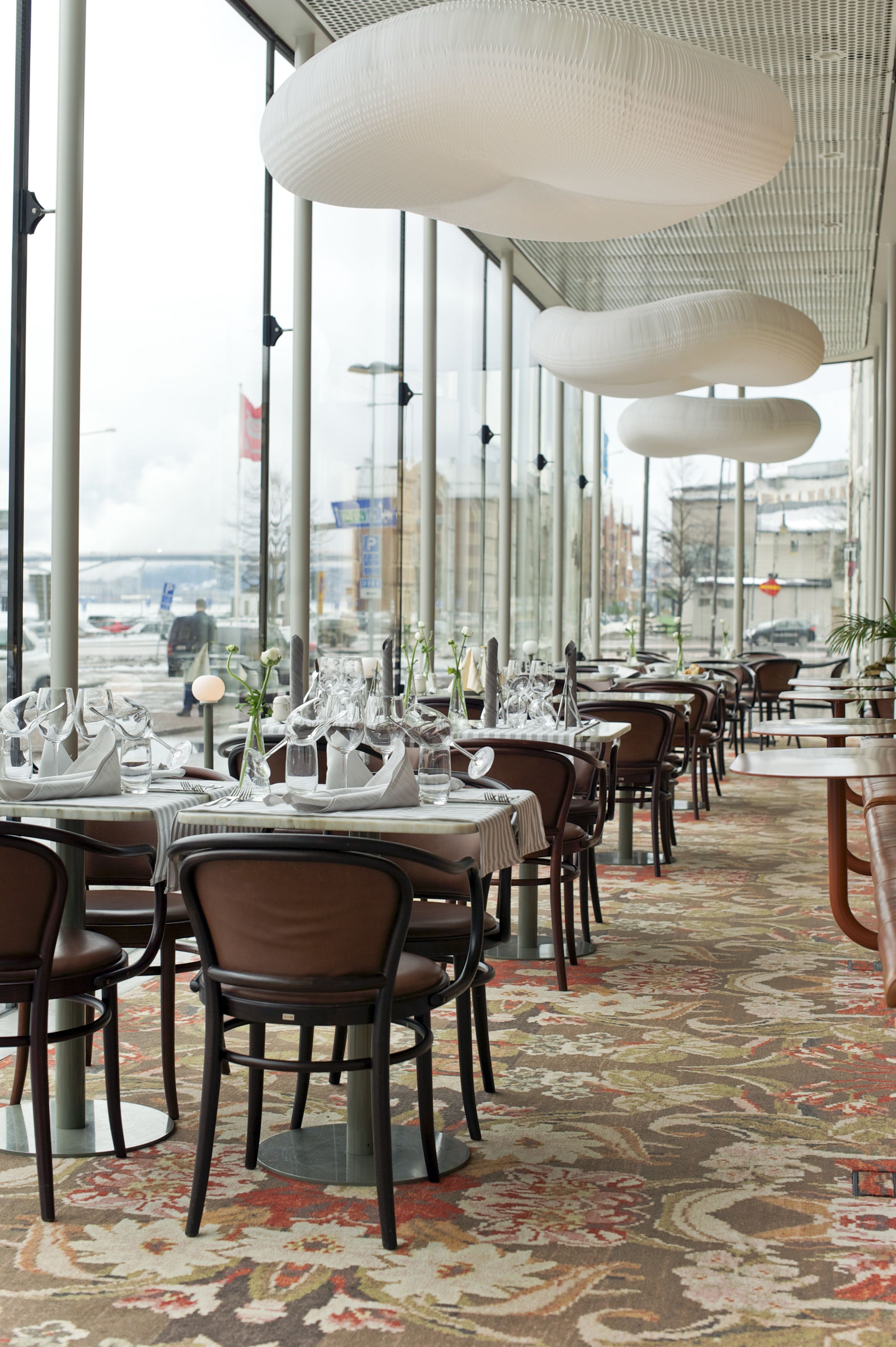 A restaurant with tables set for dining, large windows, and a view of the street.