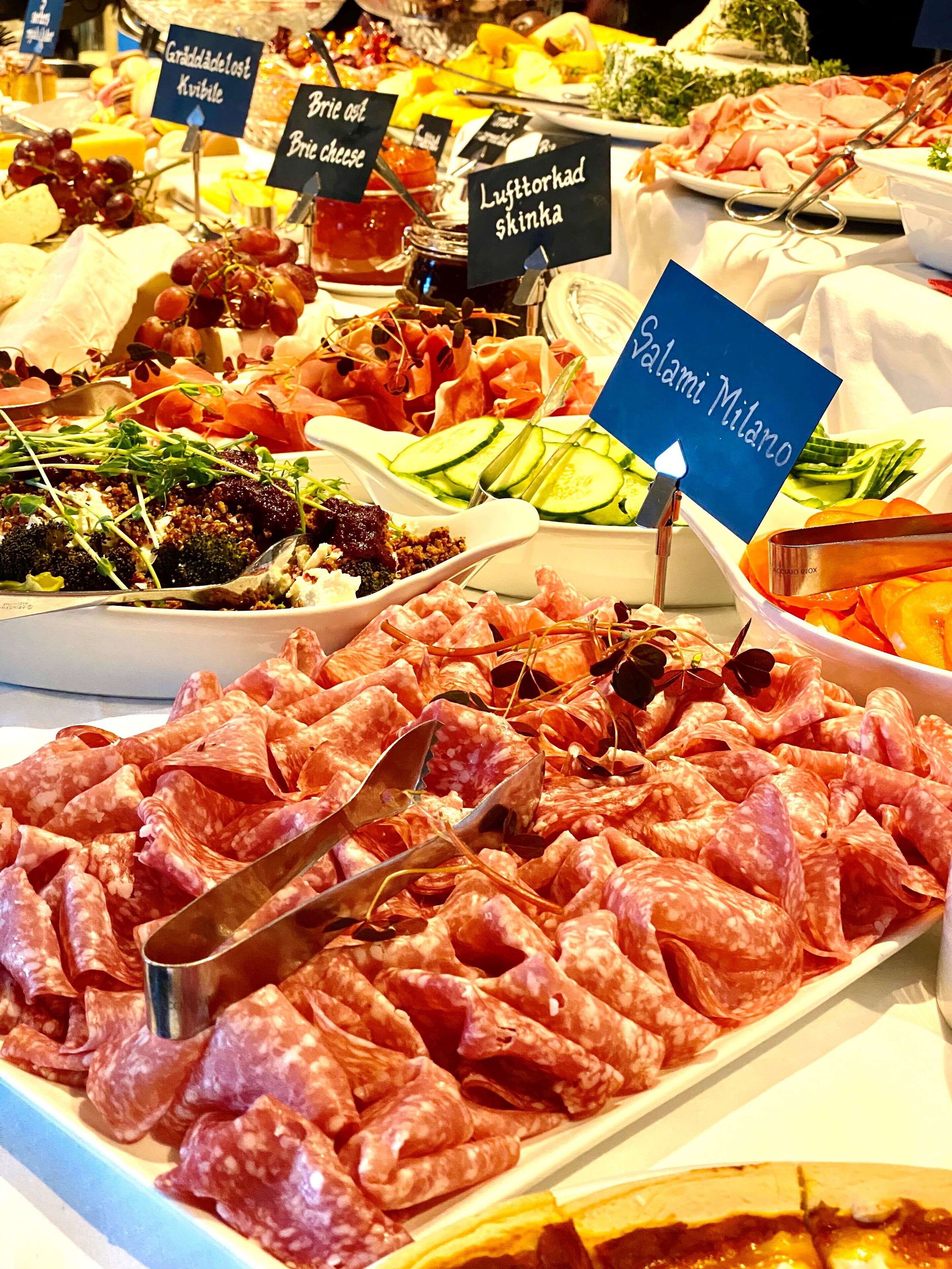 A variety of cured meats and cheeses displayed on a table with labels indicating different types.