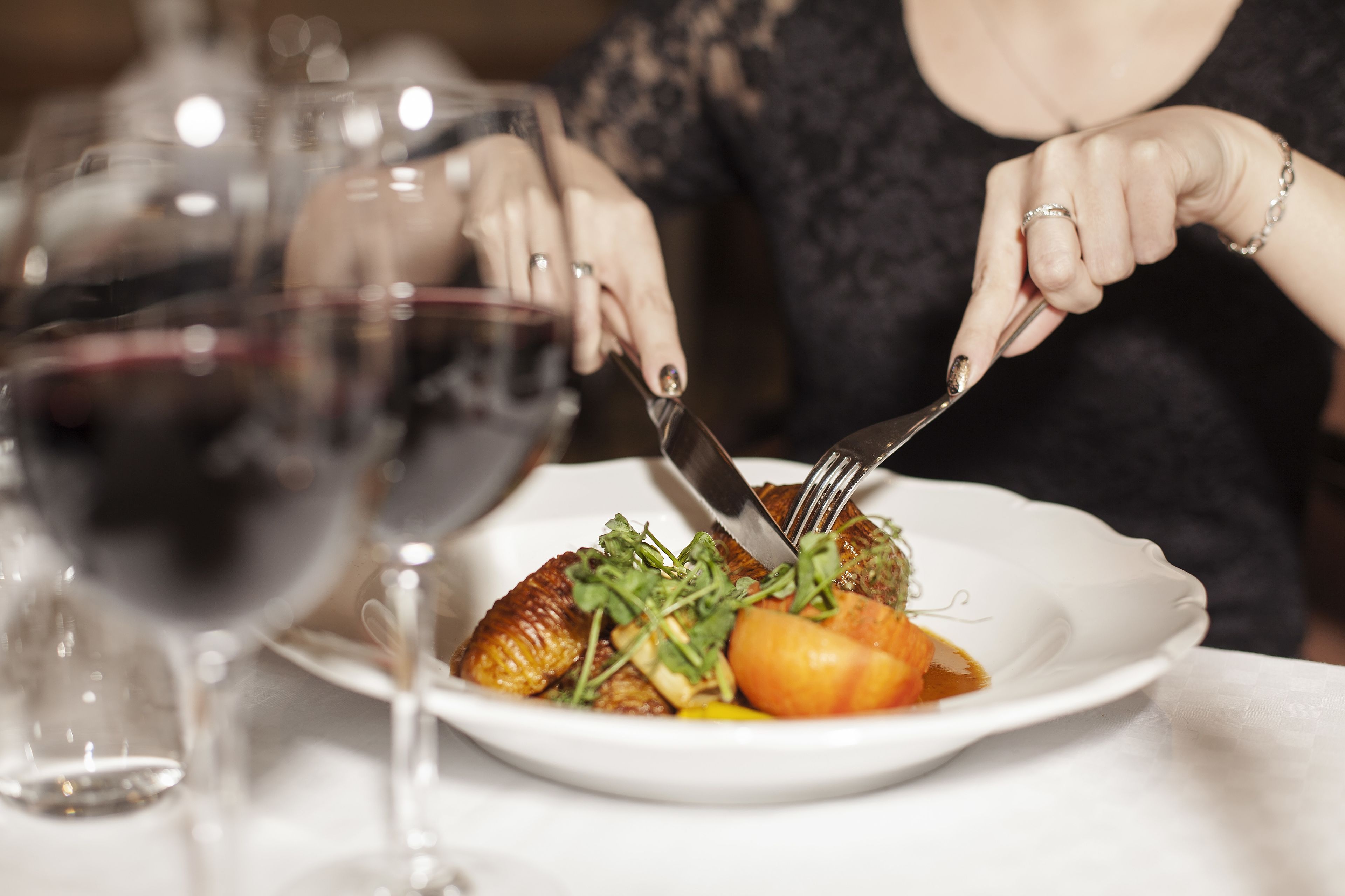 A person dining at a table with a plate of food, a wine glass, and a fork.