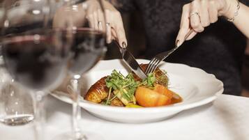 A person dining at a table with a plate of food, a wine glass, and a fork.