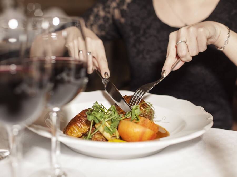 A person dining at a table with a plate of food, a wine glass, and a fork.