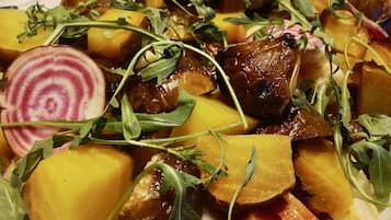 Una mesa de buffet con diversos platos, incluyendo una ensalada con rúcula y rodajas de remolacha, y un plato con calabacín y champiñones.